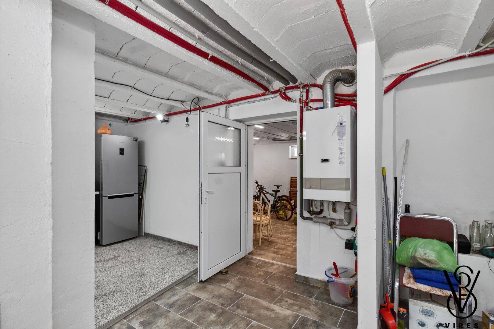 Kellerraum mit Heizungsanlage, Kühlschrank und Zugang zu weiteren Bereichen.
