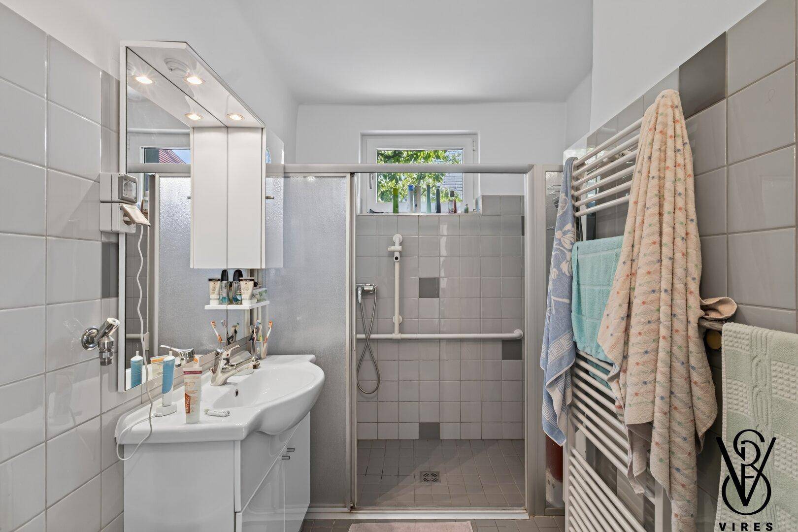 Modernes Badezimmer mit ebenerdiger Dusche, Haltegriffen und Fenster.
