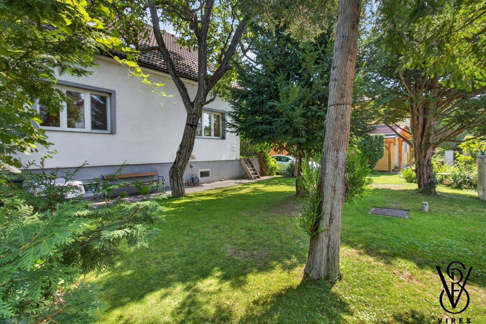 Gepflegte Rasenfläche neben dem Haus, umgeben von Bäumen und Sträuchern.