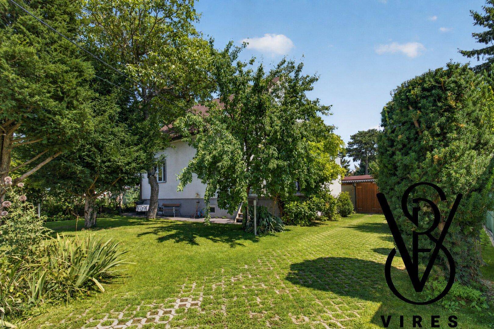 Garten mit Rasenfläche und befestigtem Bereich für Fahrzeuge.