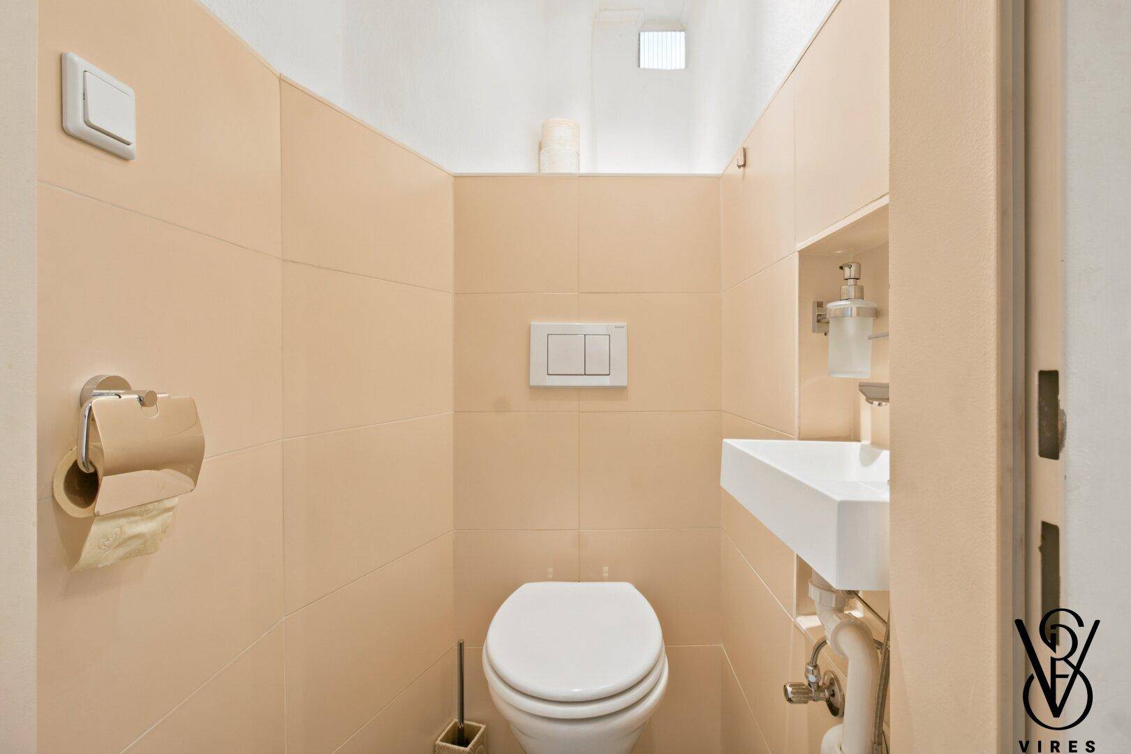 Separate Toilette mit modernem Waschbecken und beigefarbenen Fliesen.