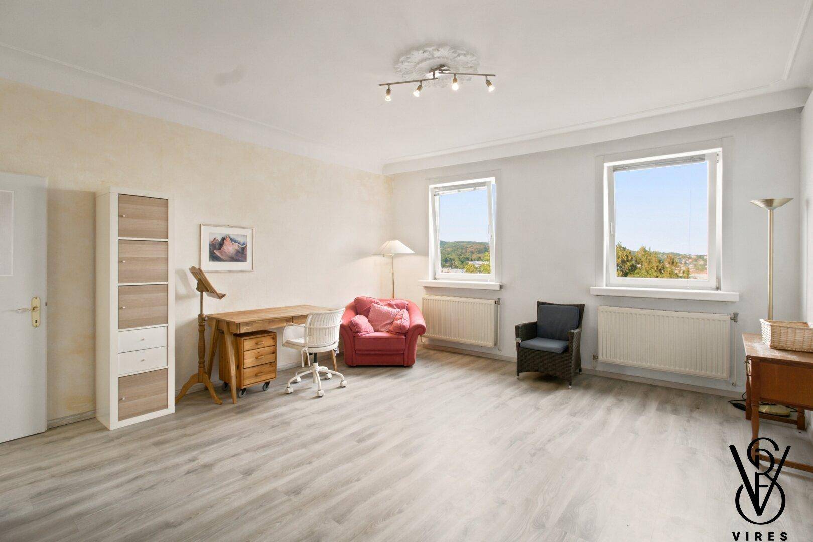 Helles Arbeitszimmer mit Laminatboden, Schreibtisch und zwei Fenstern mit Blick ins Grüne.