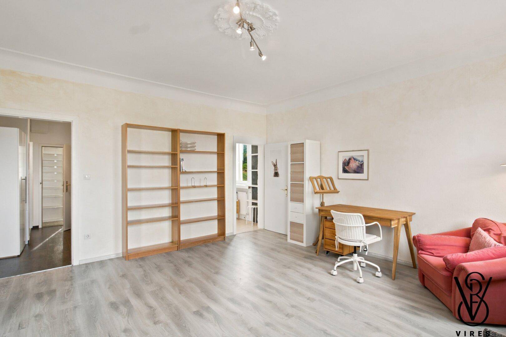 Arbeitszimmer mit Laminatboden, Bücherregal und Zugang zu weiteren Räumen.