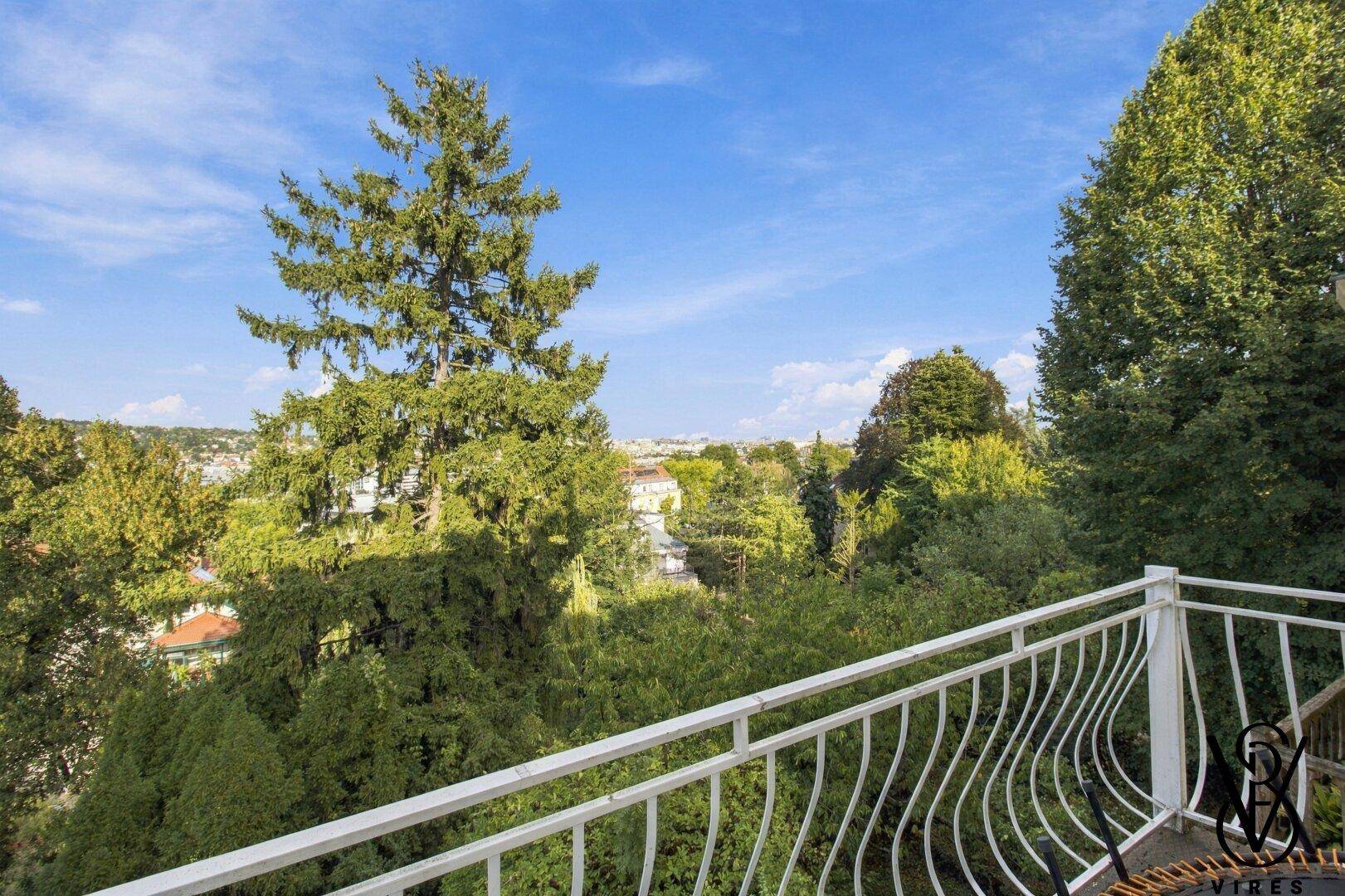 Balkon mit weißem Geländer und weitem Blick über eine grüne, bewaldete Landschaft.