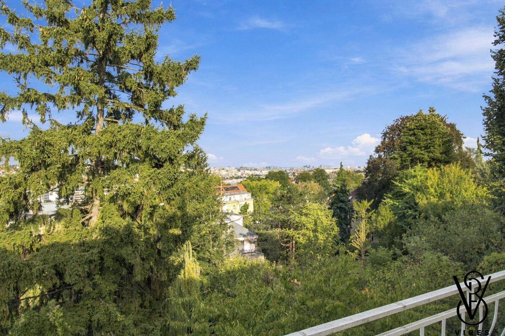 Weitläufiger Ausblick von einem Balkon auf eine grüne Umgebung mit Bäumen und Häusern.