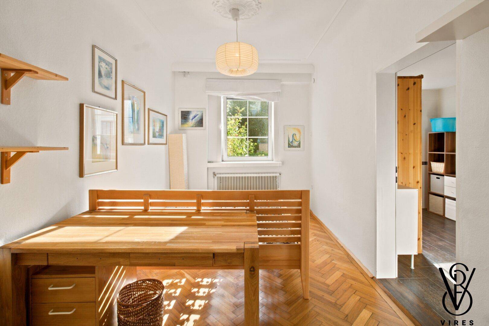 Schlafzimmer mit Holzbett, Parkettboden und einem Fenster, das viel Sonnenlicht hereinlässt.