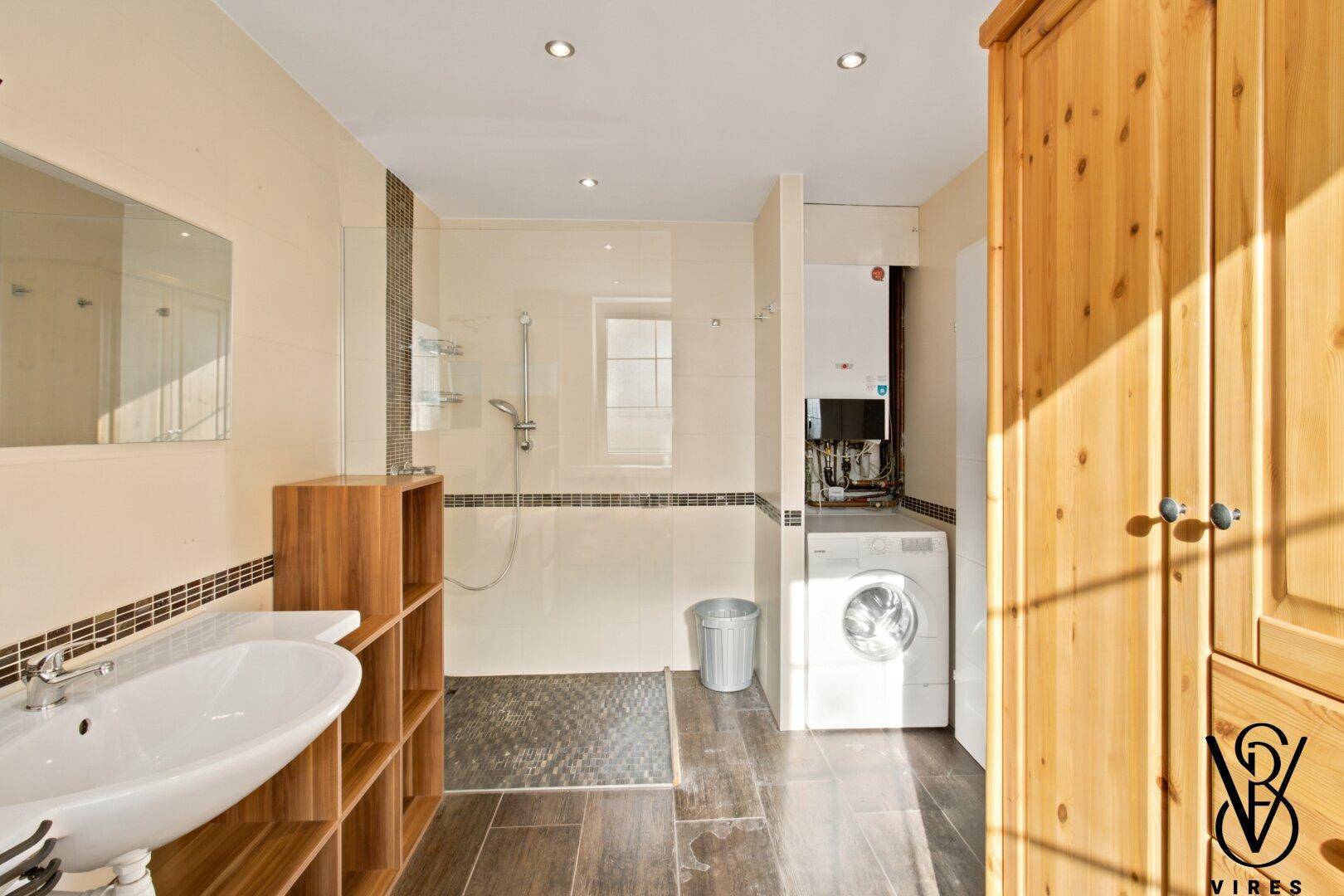 Modernes Badezimmer mit ebenerdiger Dusche, Waschmaschine und Holzschrank.