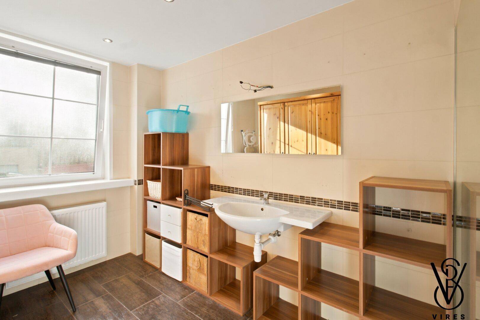 Geräumiges Badezimmer mit Waschbecken, Holzregalen und einem großen Fenster.