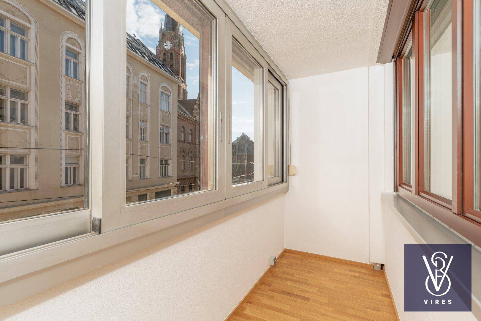 Geschlossene Loggia mit Holzboden und Blick auf die umliegenden Stadtgebäude.