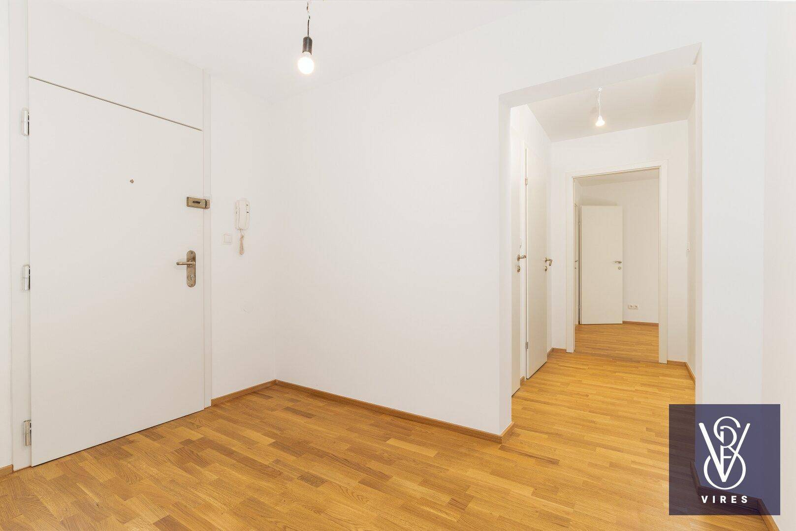 Heller Eingangsbereich mit Holzboden, weiß gestrichenen Wänden und Gegensprechanlage.