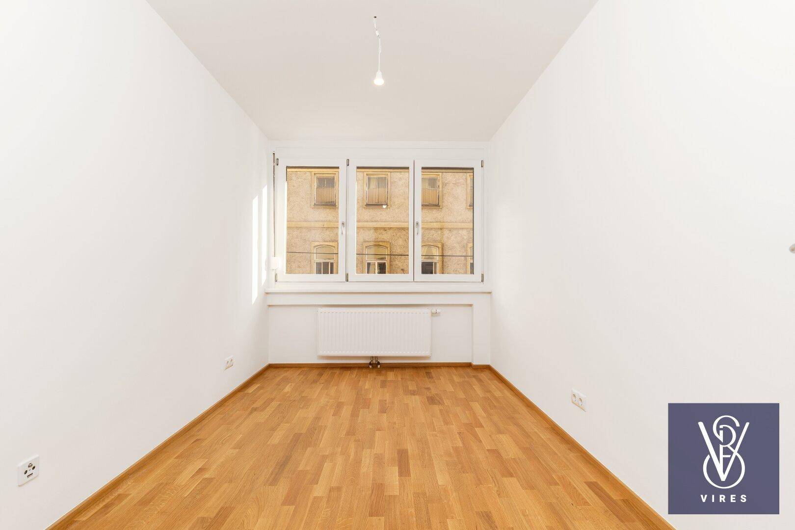 Helles, leeres Zimmer mit Parkettboden und Fensterfront, ideal als Schlaf- oder Arbeitszimmer.