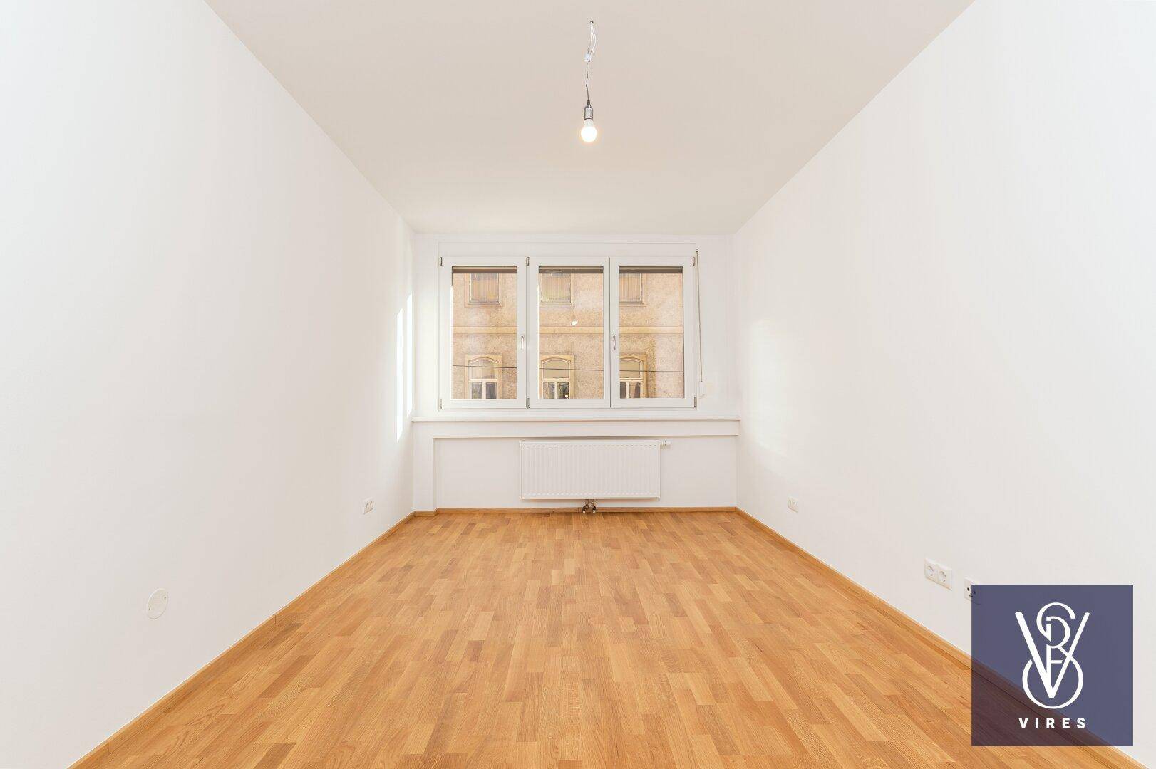 Geräumiges, helles Schlafzimmer mit Parkettboden und Blick auf die umliegenden Gebäude.