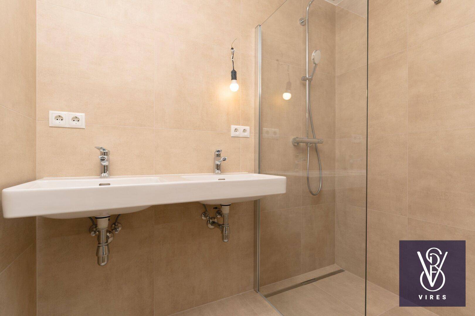 Modernes Badezimmer mit beigefarbenen Fliesen, Doppelwaschbecken und einer begehbaren Dusche.