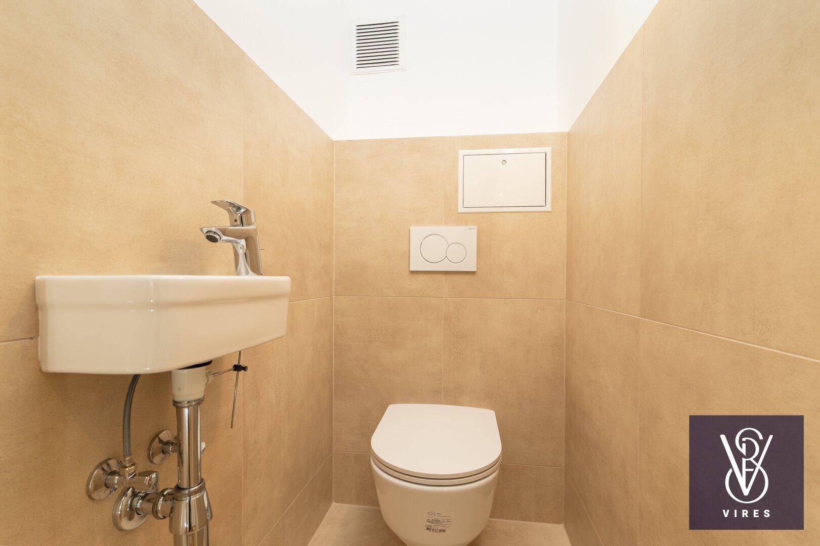 Kleines, gefliestes Gäste-WC mit modernem Wand-WC und Handwaschbecken.