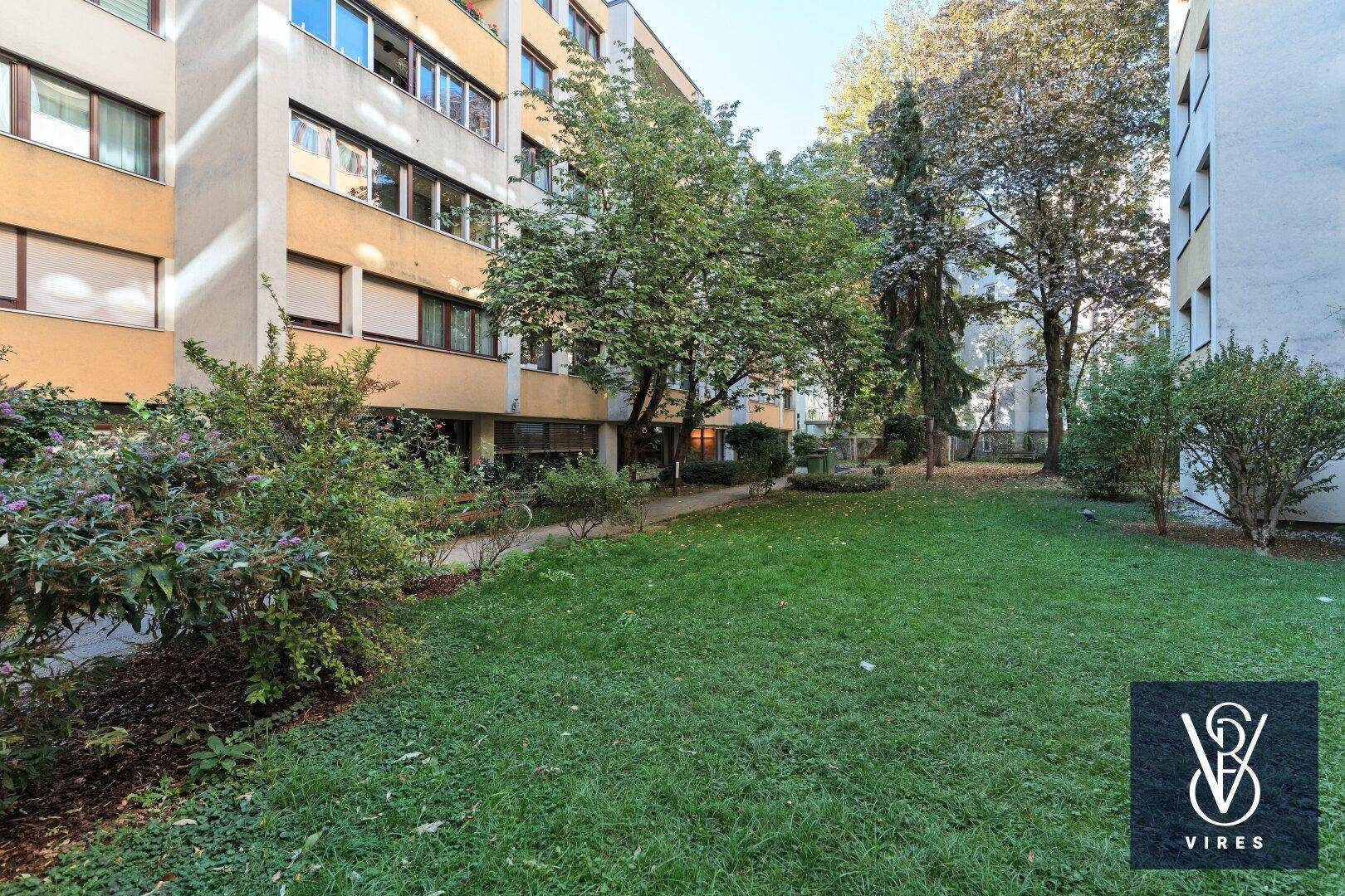 Gepflegte Gemeinschaftsgartenanlage mit Rasenflächen und Bäumen zwischen den Wohngebäuden.