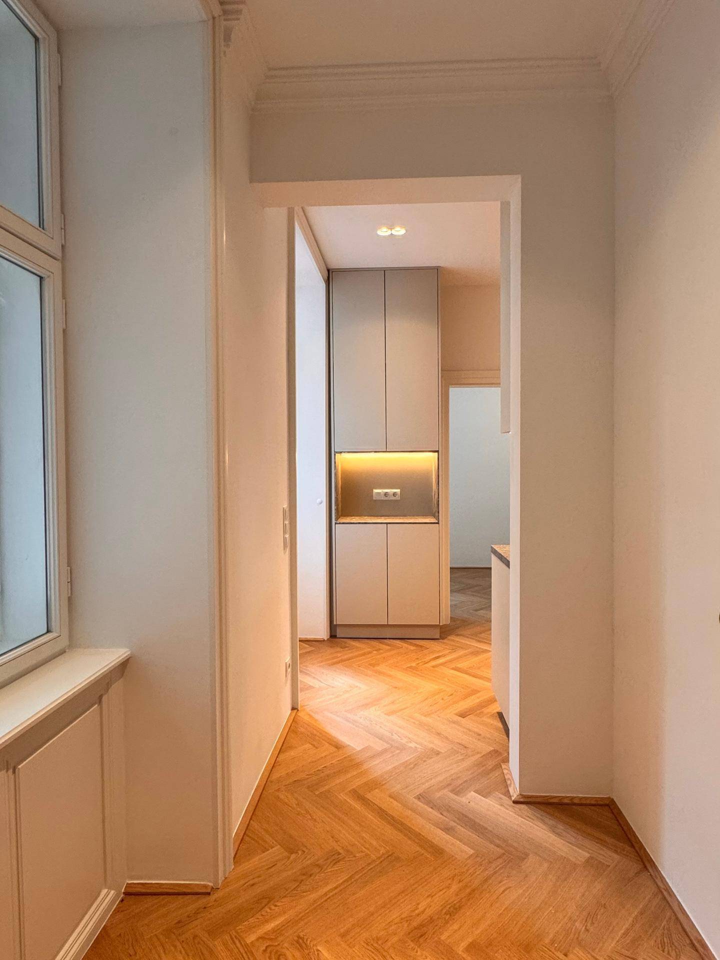 Heller Flur mit Fischgrätparkettboden, hohen Decken und modernem Einbauschrank.