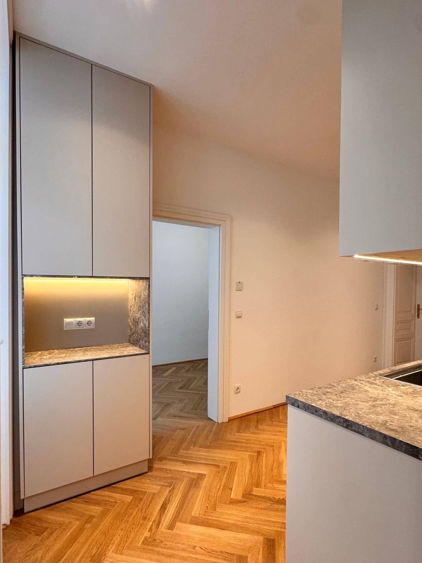Moderne Einbauküche mit beleuchteter Nische, eleganten Arbeitsplatten und Fischgrätparkettboden.