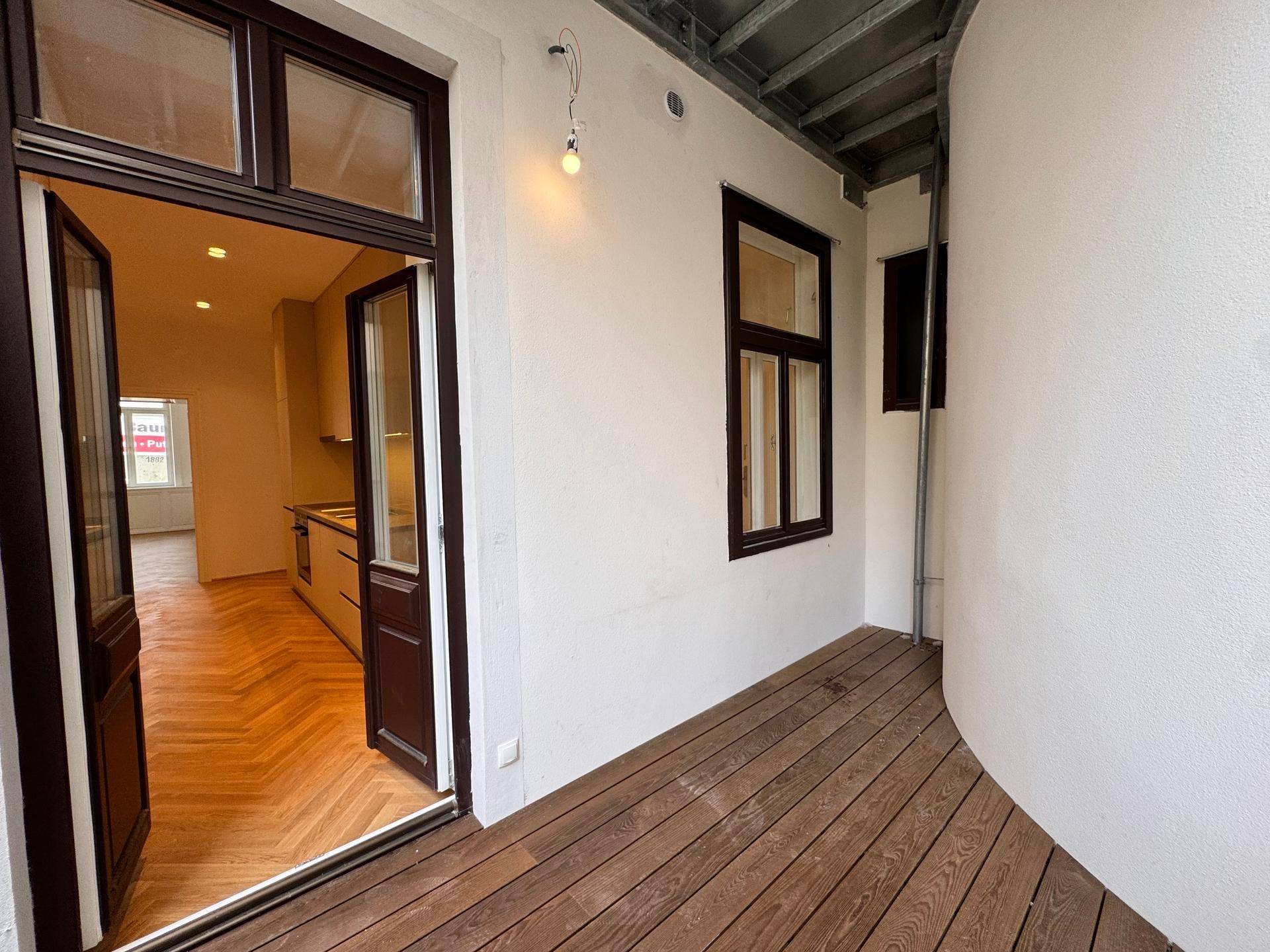 Überdachte Loggia mit Holzboden und direktem Zugang zur modernen Küche.
