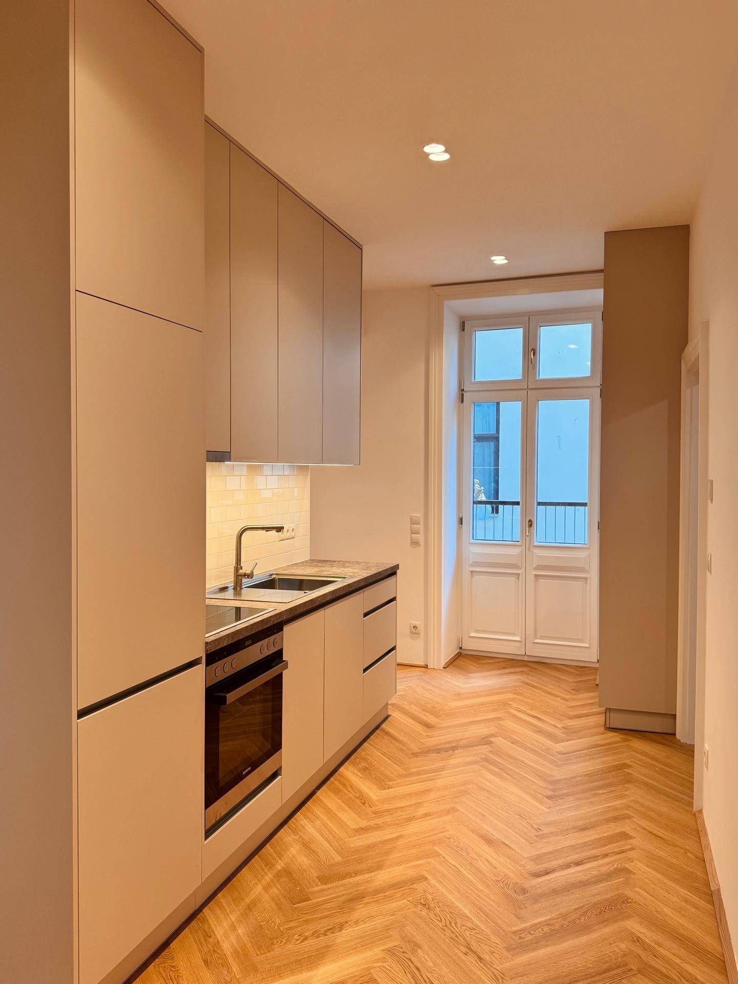 Lichtdurchflutete moderne Küche mit Einbaugeräten, Fischgrätparkett und französischem Balkon.