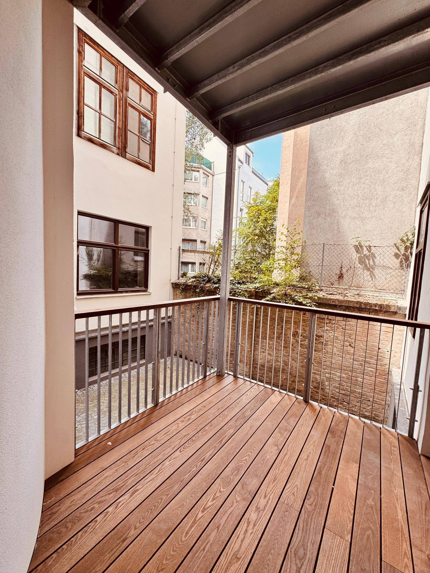 Geräumiger Balkon mit Holzdielen und Blick auf die umliegenden Gebäude und Bäume.