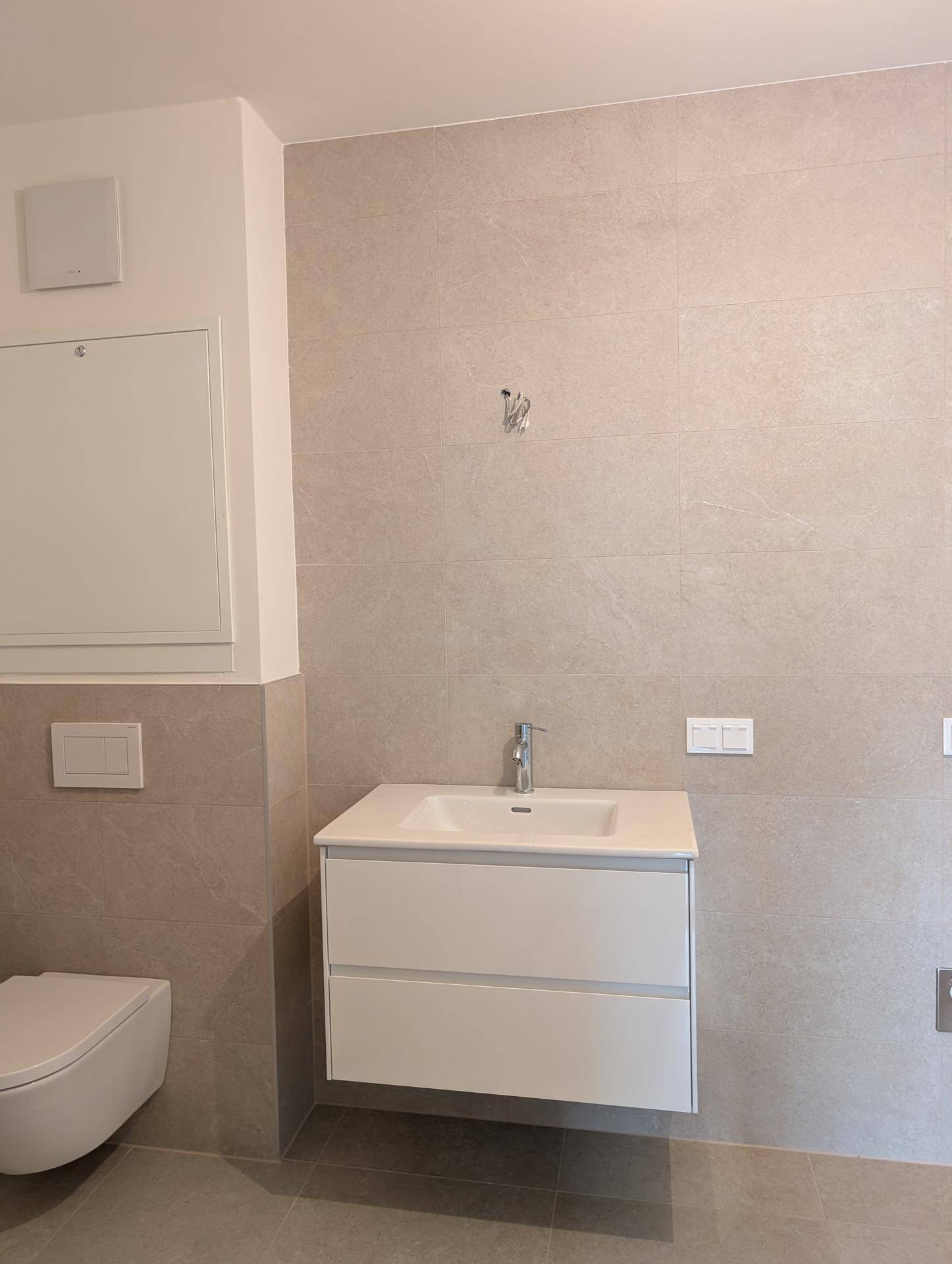 Modernes Badezimmer mit schwebendem Waschtisch, grauen Fliesen und Wand-WC.