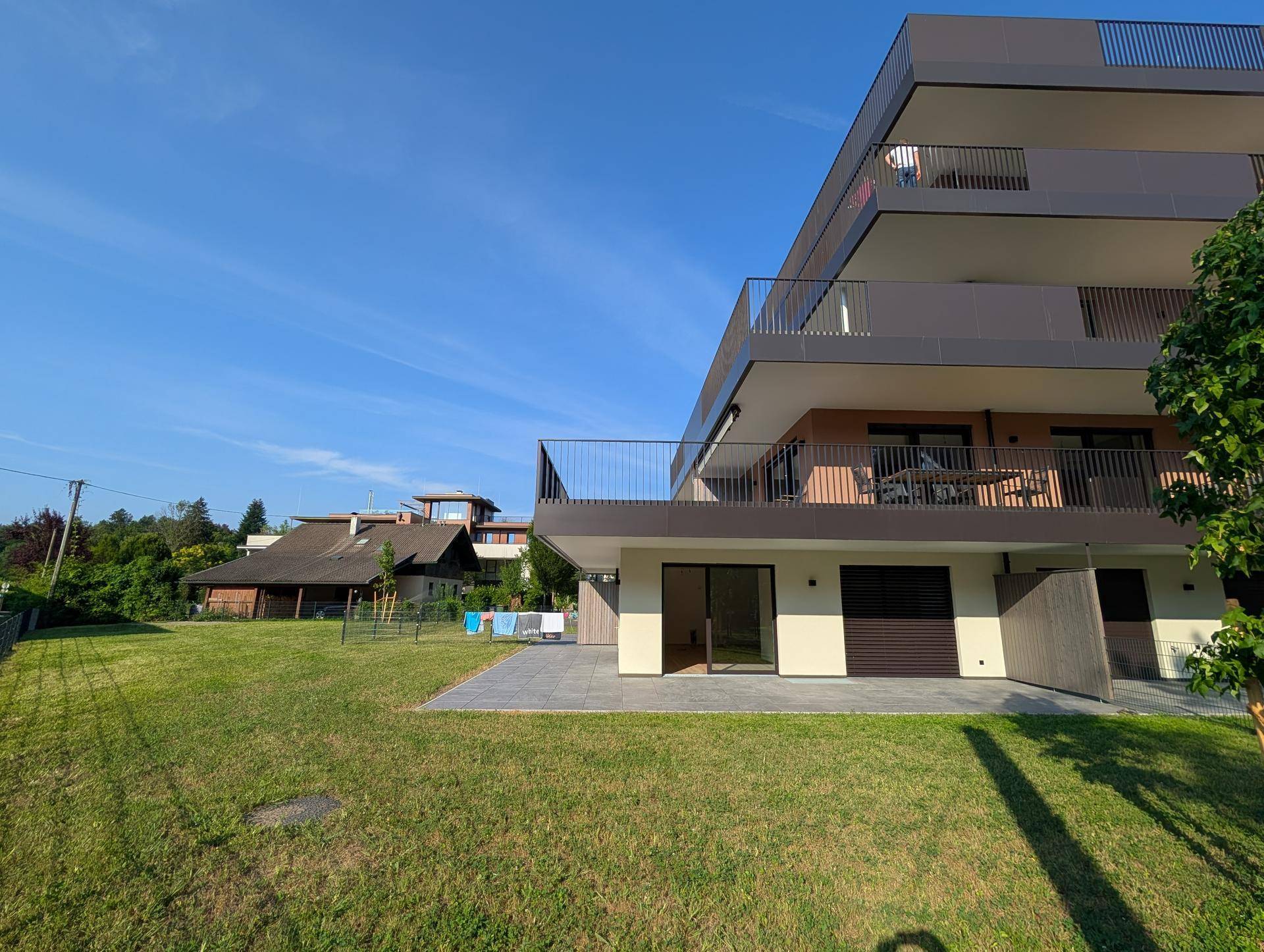 Seitenansicht des modernen Gebäudes mit einer gepflasterten Terrasse und einer grünen Rasenfläche.