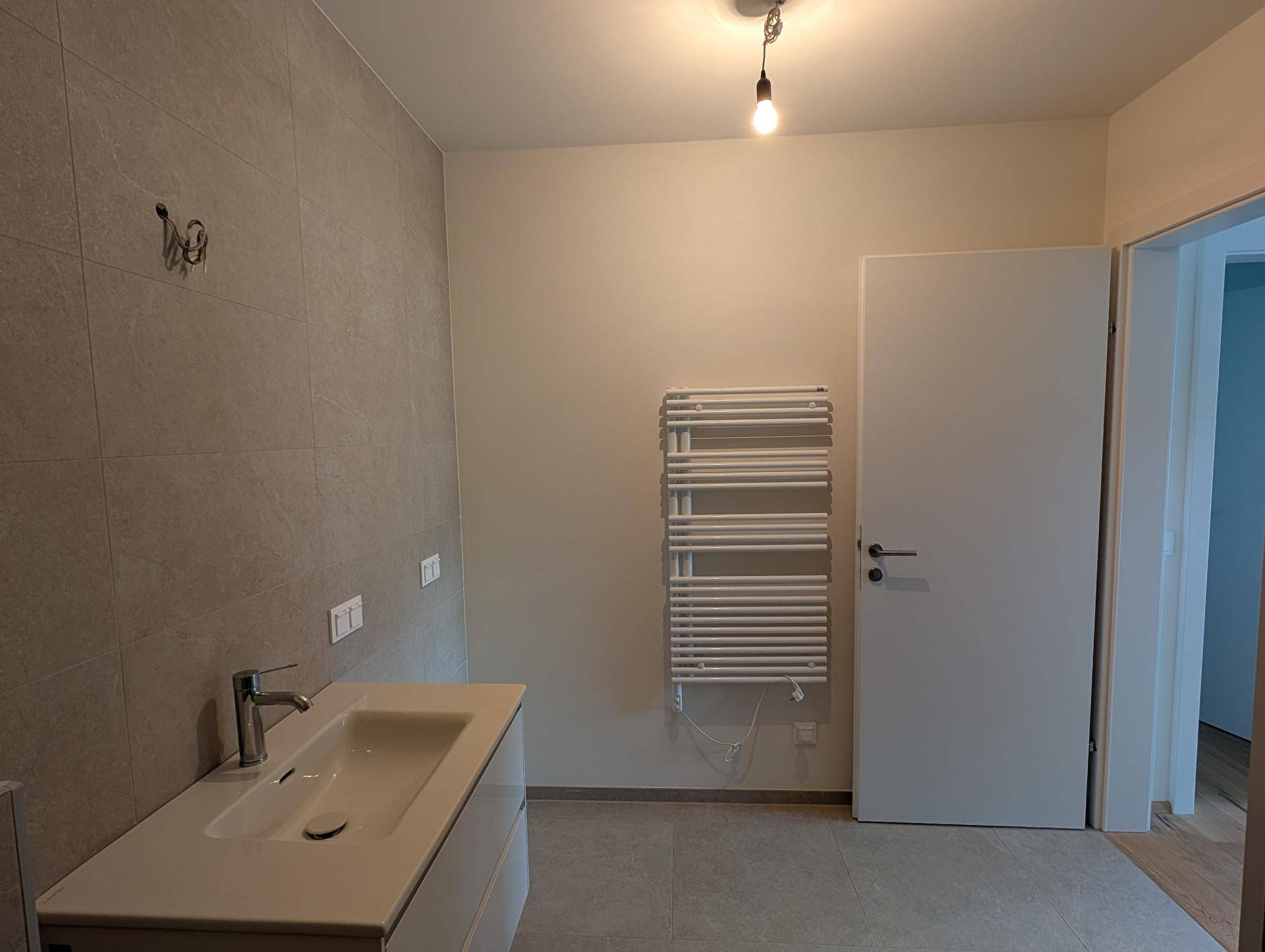Helles Badezimmer mit Waschtisch, beheiztem Handtuchhalter und grauen Fliesen.