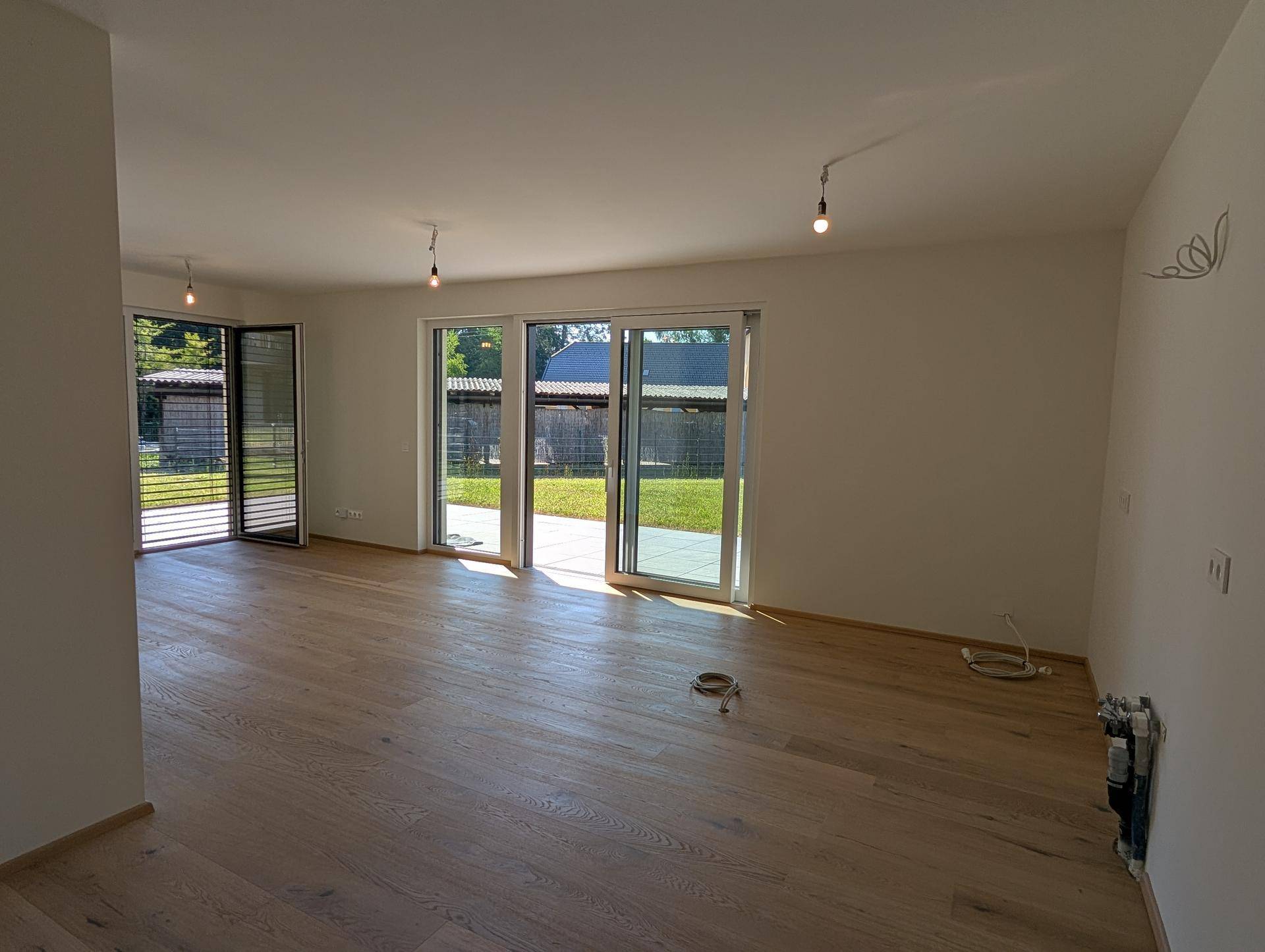 Geräumiges Wohnzimmer mit hellem Holzboden und Zugang zu einer Außenterrasse.