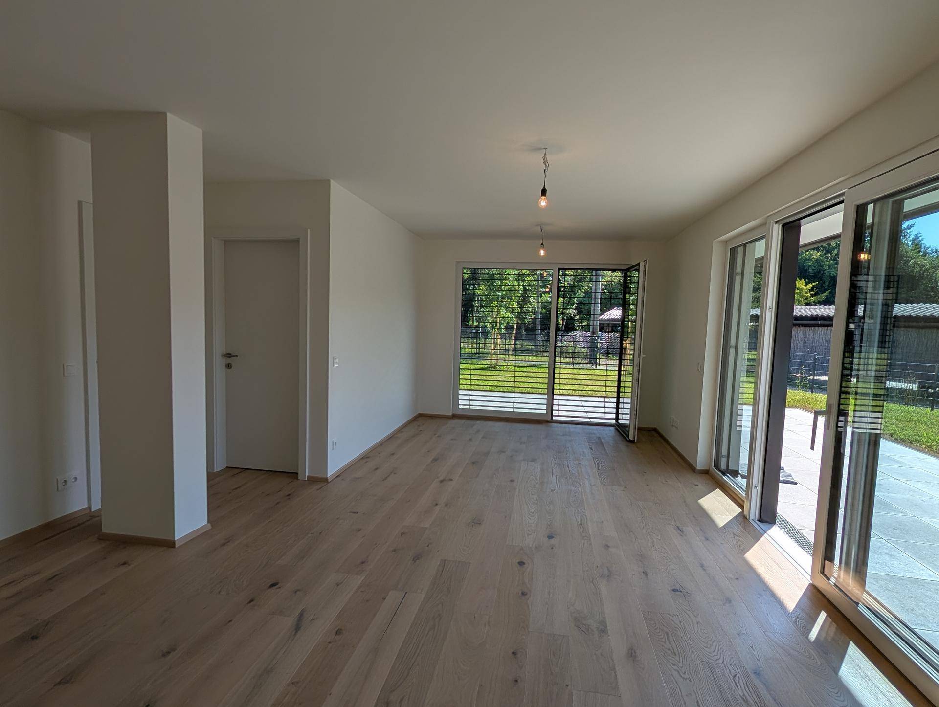 Helles, leeres Wohnzimmer mit Holzboden und großen Schiebetüren zum Garten.