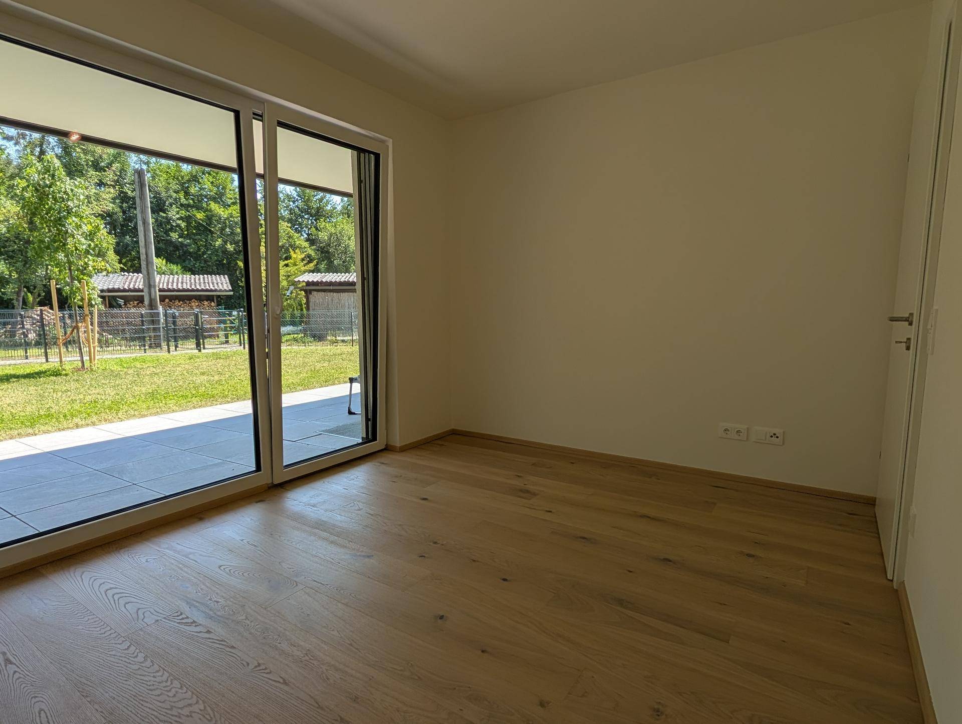 Helles Schlafzimmer mit Holzboden und großen Schiebetüren zum Außenbereich.