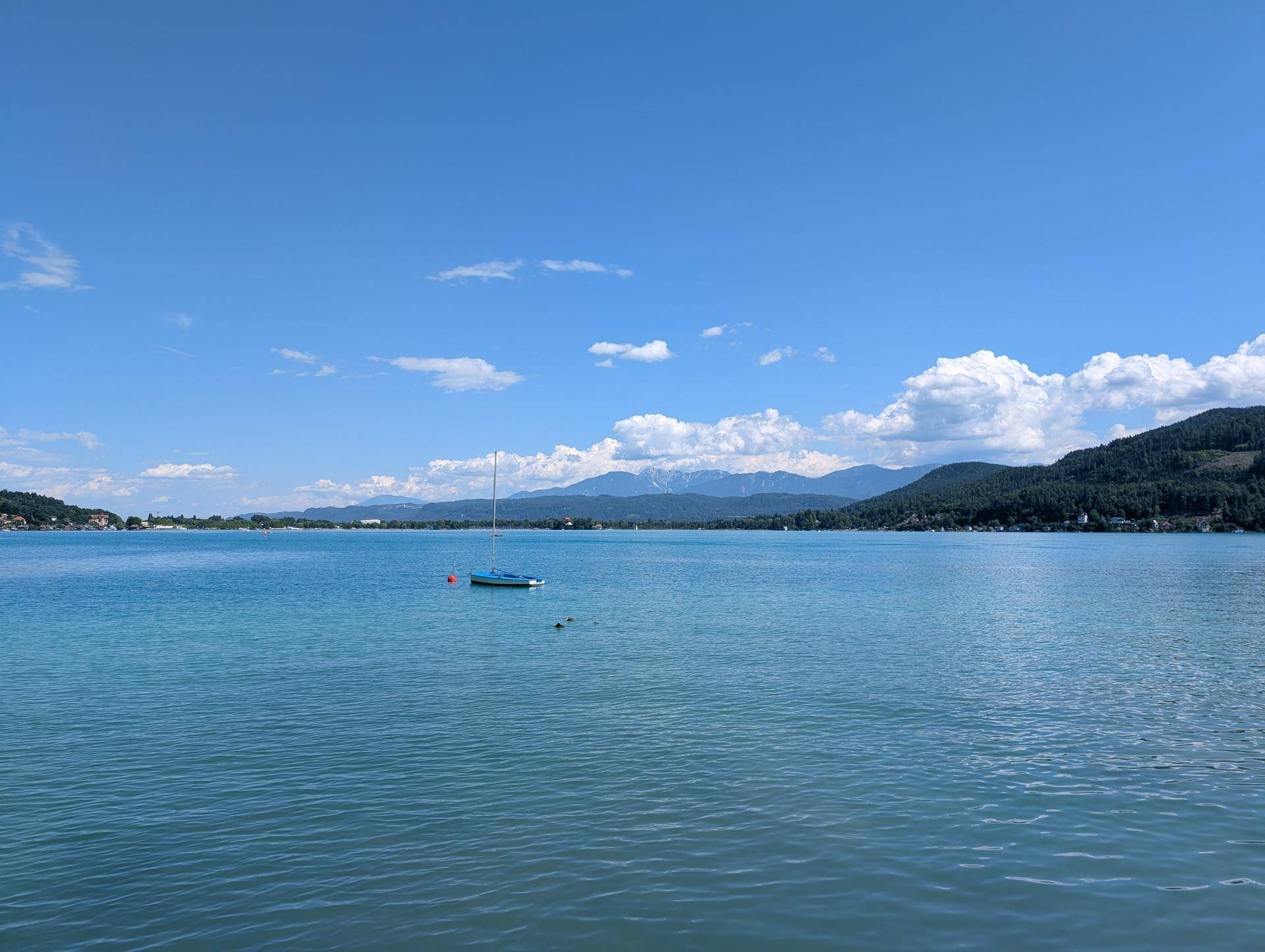 Weitläufiger Blick über den blauen Wörthersee mit Bergen im Hintergrund unter klarem Himmel.