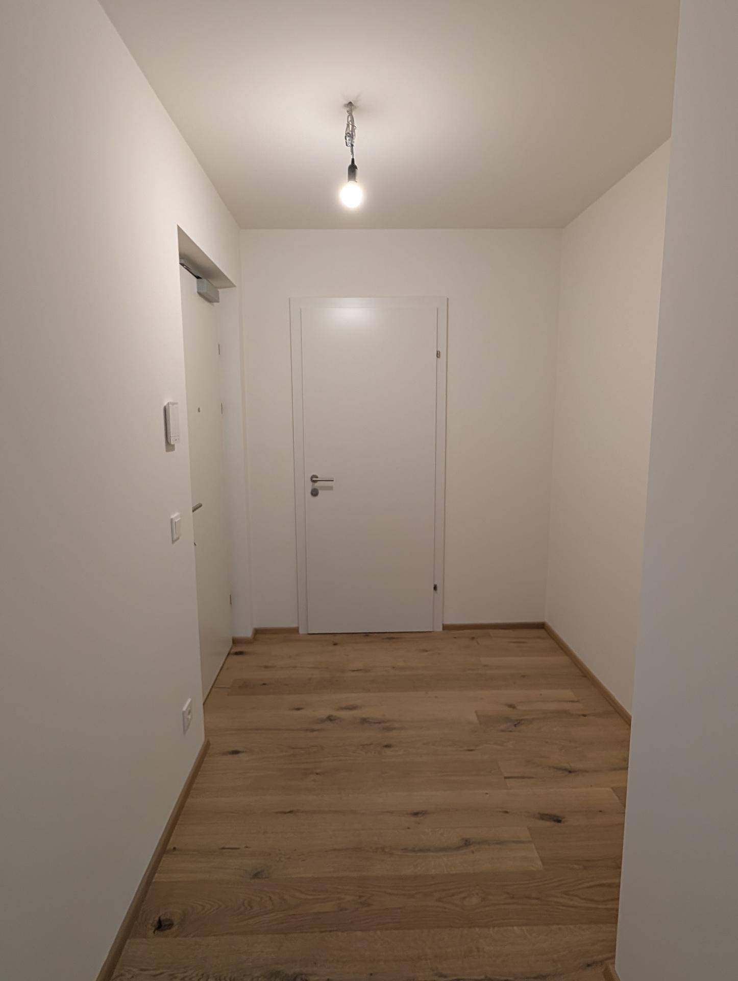 Heller Flur mit Holzboden und weißen Wänden, der zu den Zimmern führt.