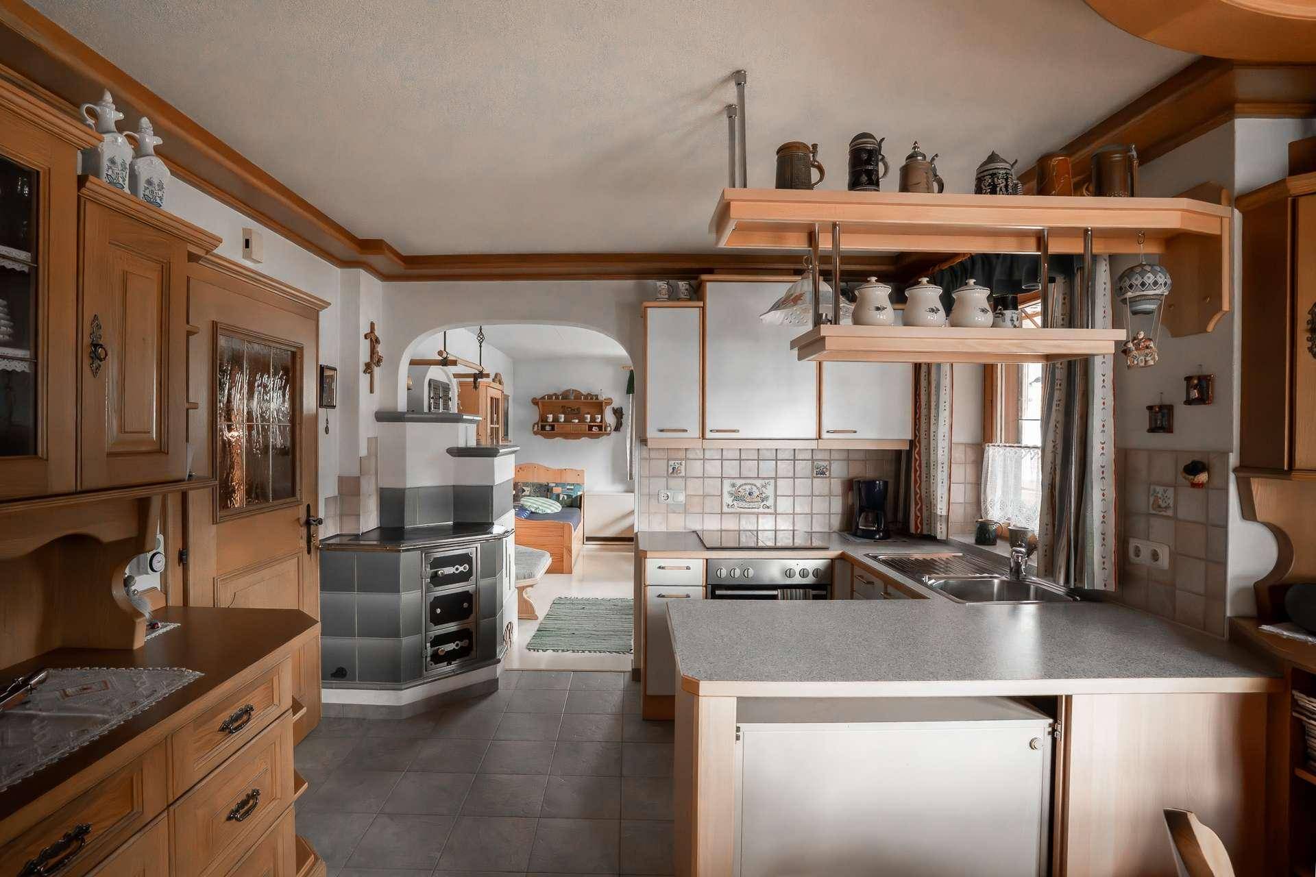 Große traditionelle Küche mit Kachelofen, Holzmöbeln und Fliesenboden.