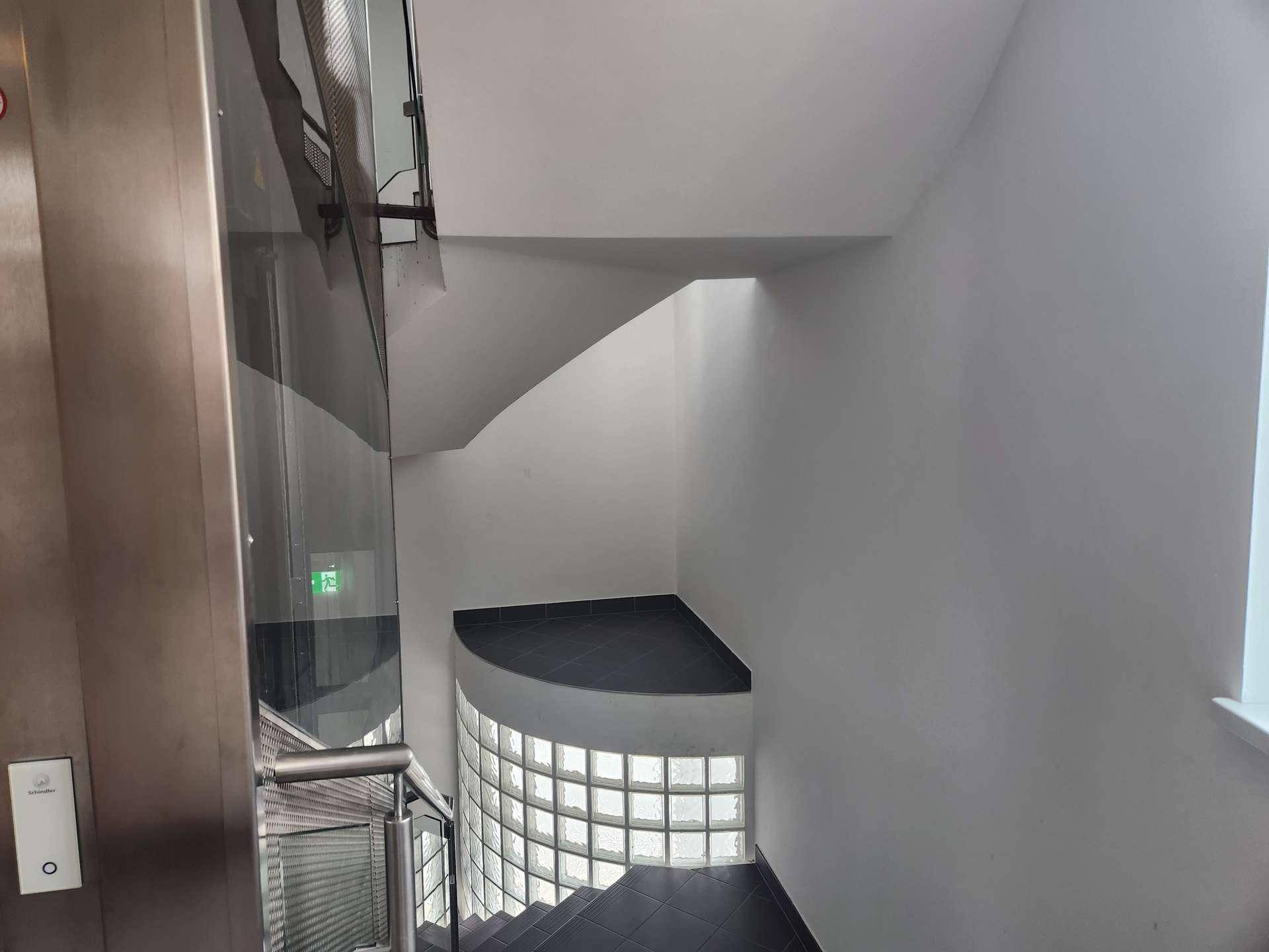 Modernes Treppenhaus mit Glasaufzug und einer stilvollen Glasbausteinwand, die für Helligkeit sorgt.