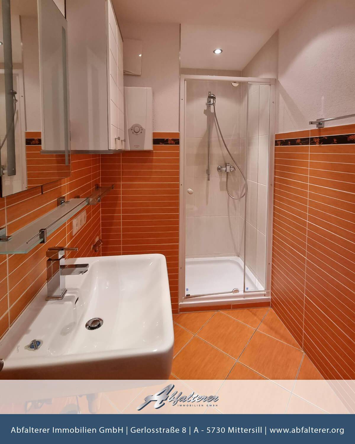 Badezimmer mit orangefarbenen Fliesen, Duschkabine und Einzelwaschbecken mit Spiegelschrank.