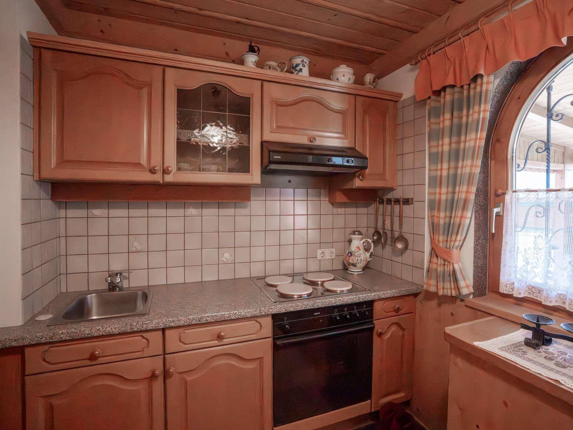 Kleine traditionelle Küche mit Holzschränken, Fliesenrückwand und Bogenfenster.