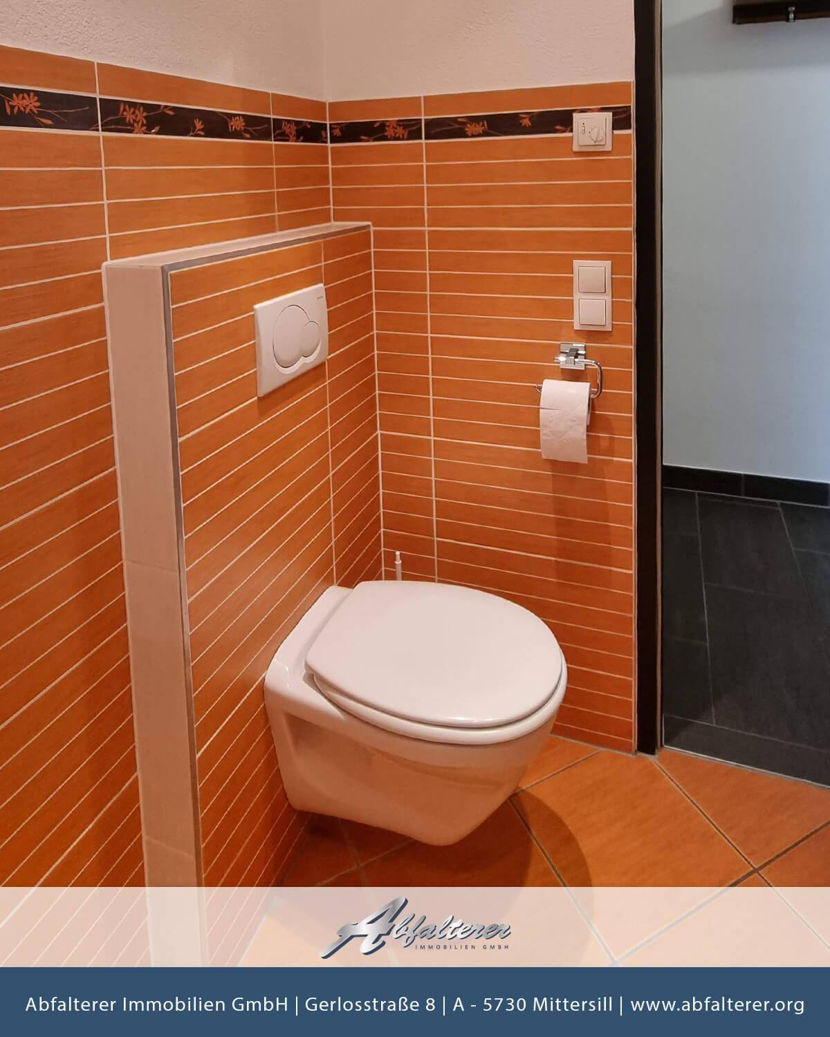 Separate Toilette mit orangefarbenen Fliesen an Wänden und Boden.