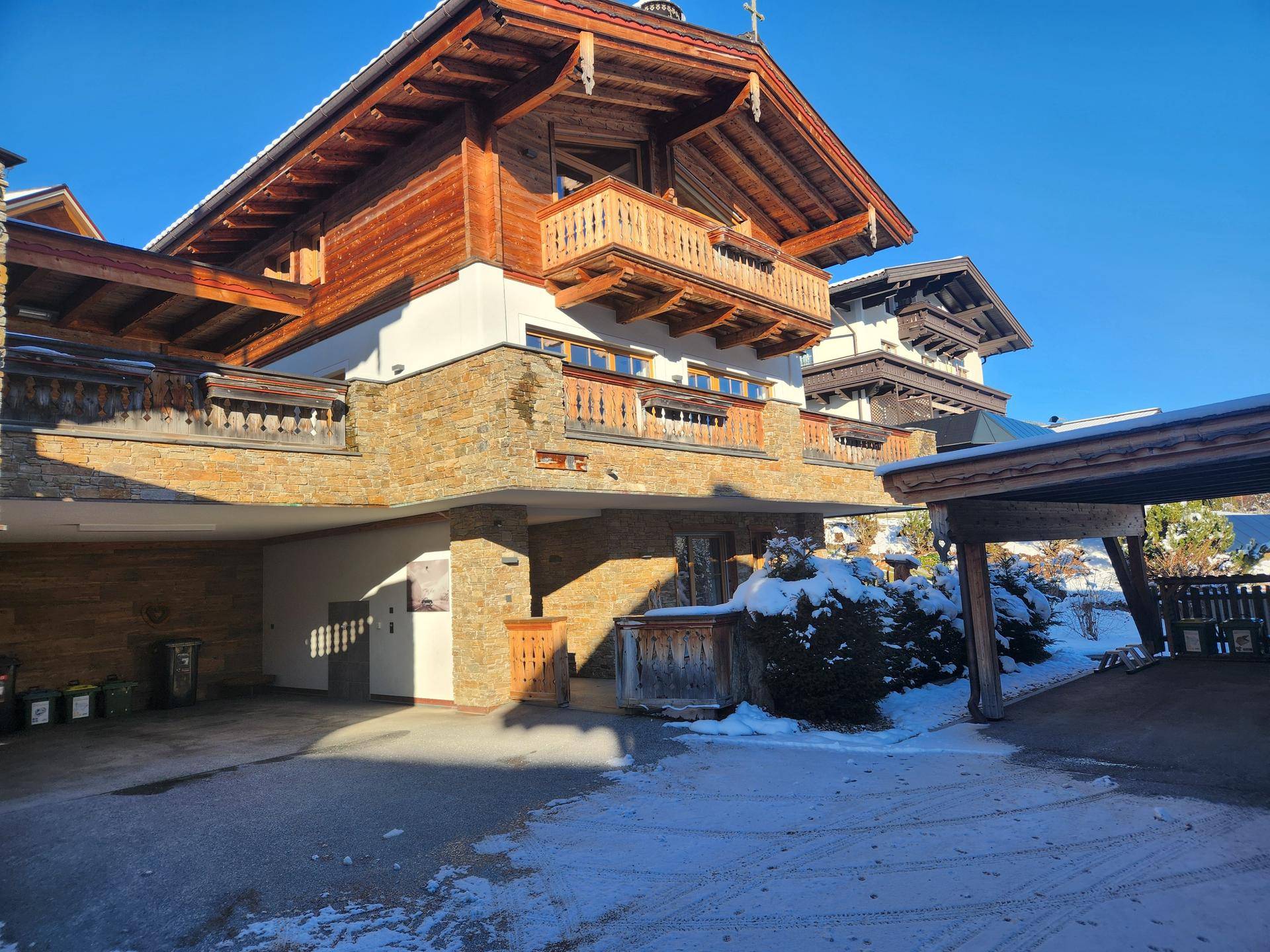 Chalet-Gebäude mit Holzfassade, Steinmauern und überdachtem Parkplatz im Winter.