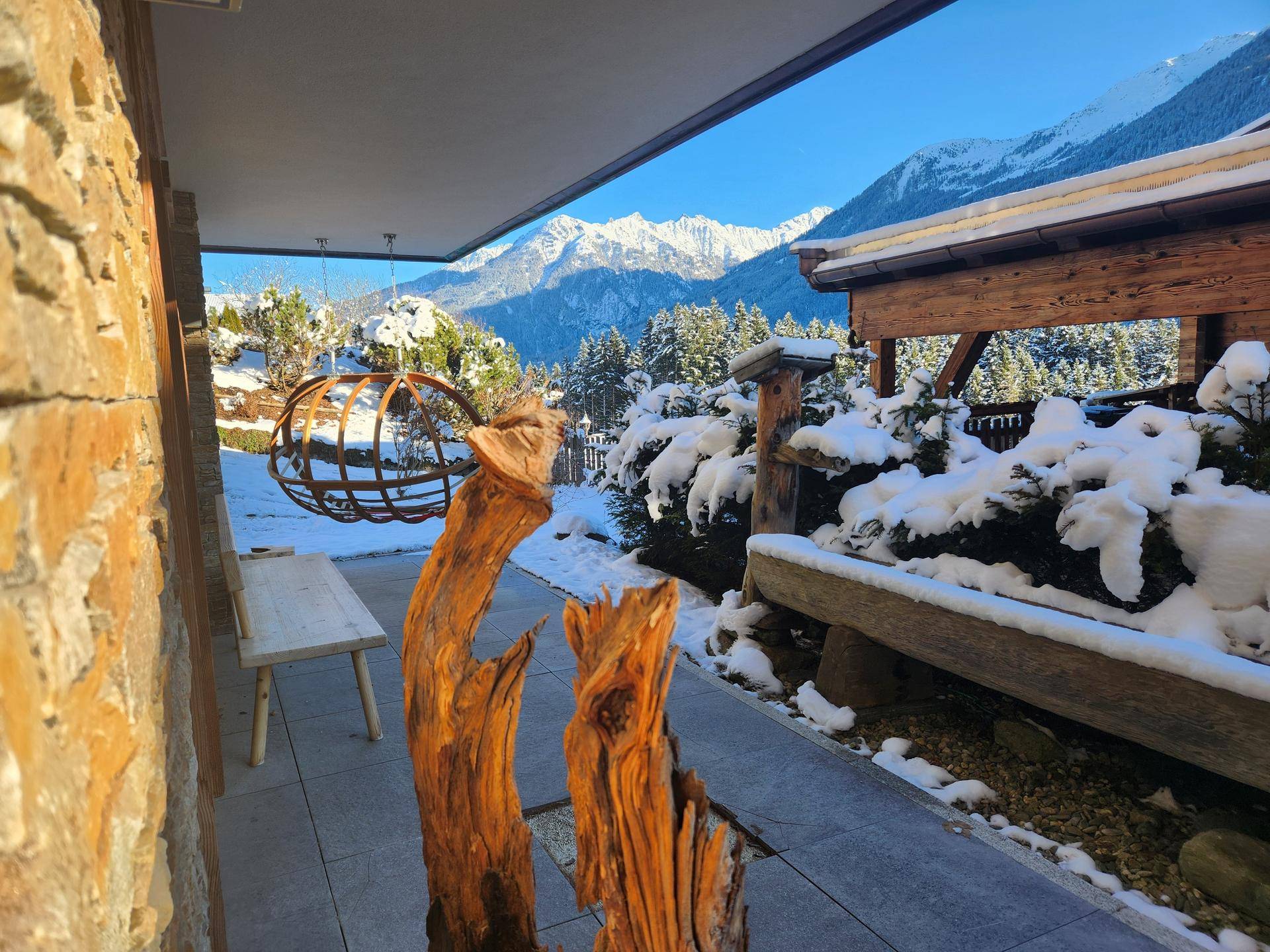 Überdachte Terrasse mit rustikaler Holzbank und Blick auf die verschneite Berglandschaft.