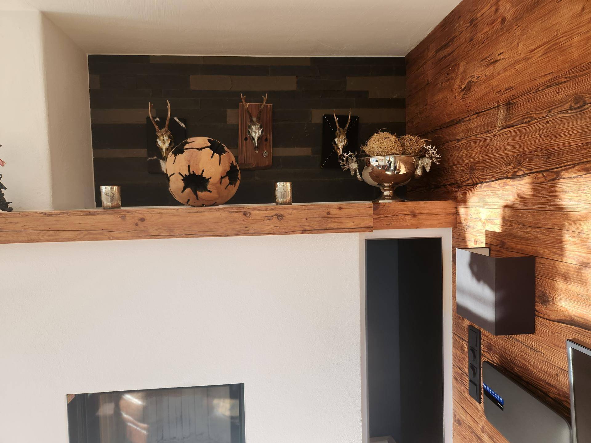 Detailansicht des Wohnzimmers mit Holzwand, alpiner Dekoration und modernem Kamin.