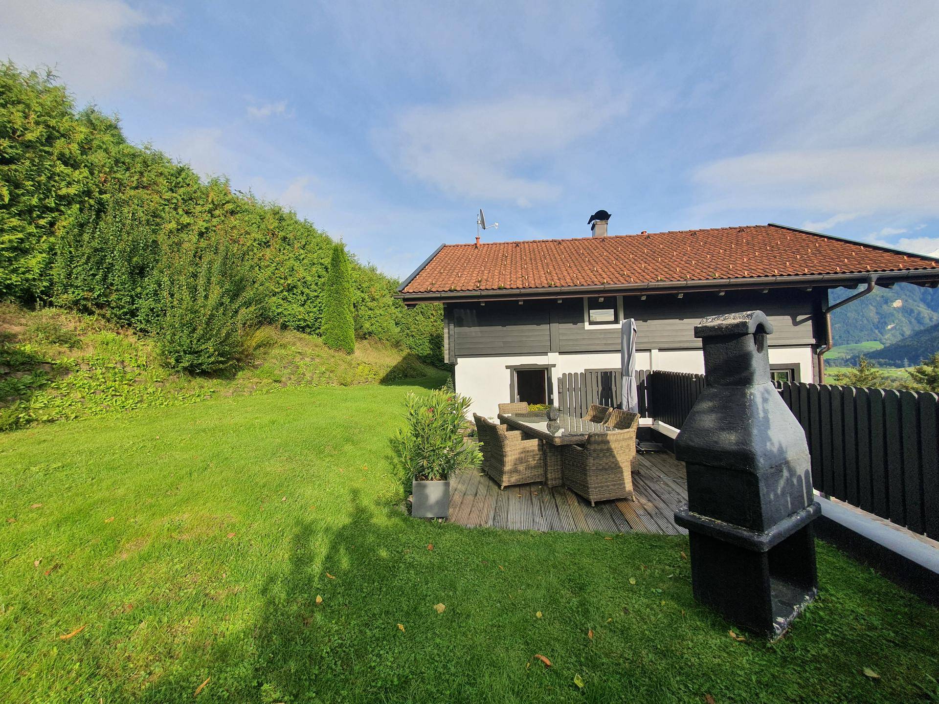 Großer Garten mit Holzterrasse, Grillplatz und Sitzgelegenheiten, umgeben von viel Grün.