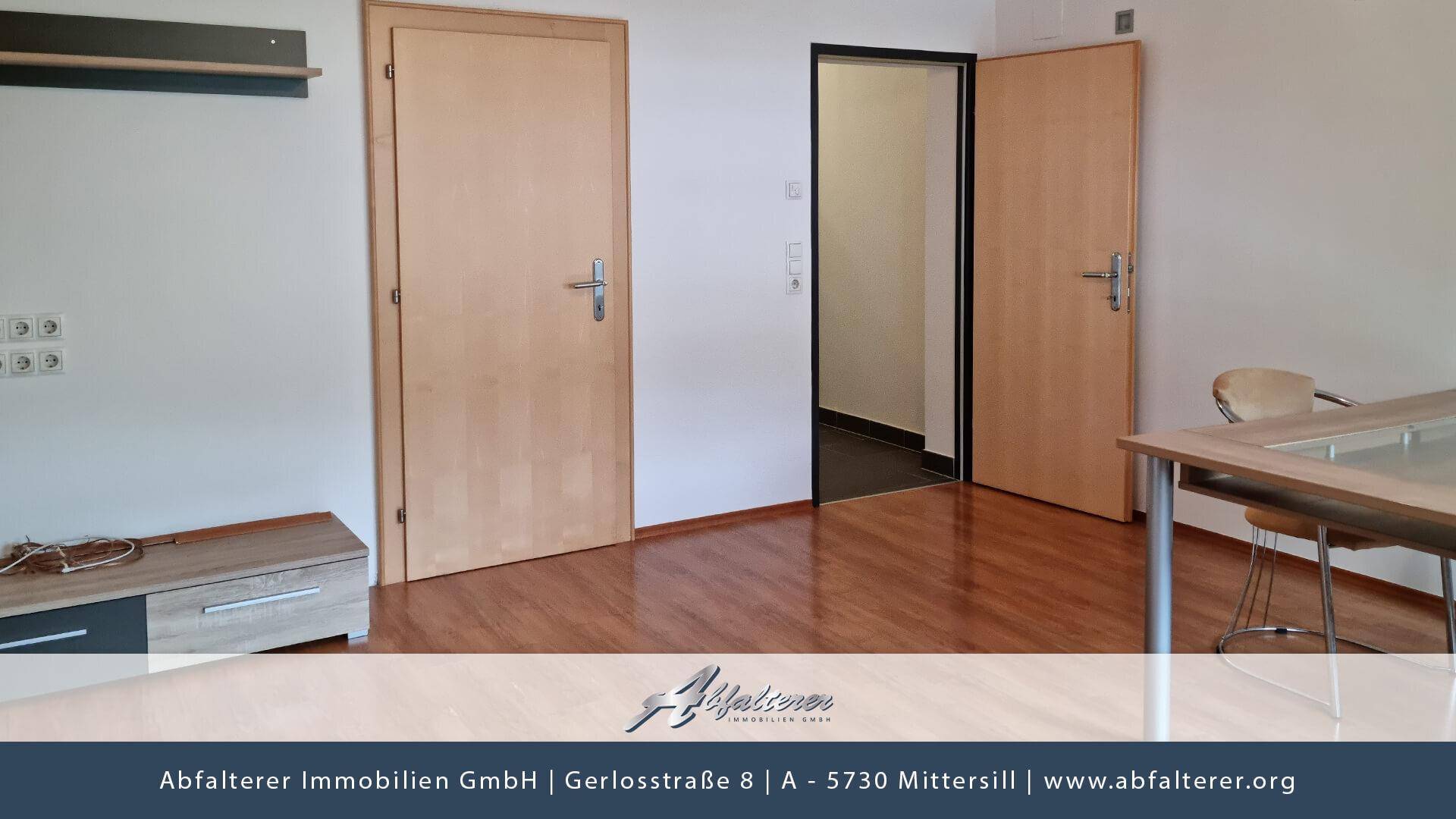Raum mit Holzboden und zwei Holztüren, der Zugang zu weiteren Bereichen bietet.