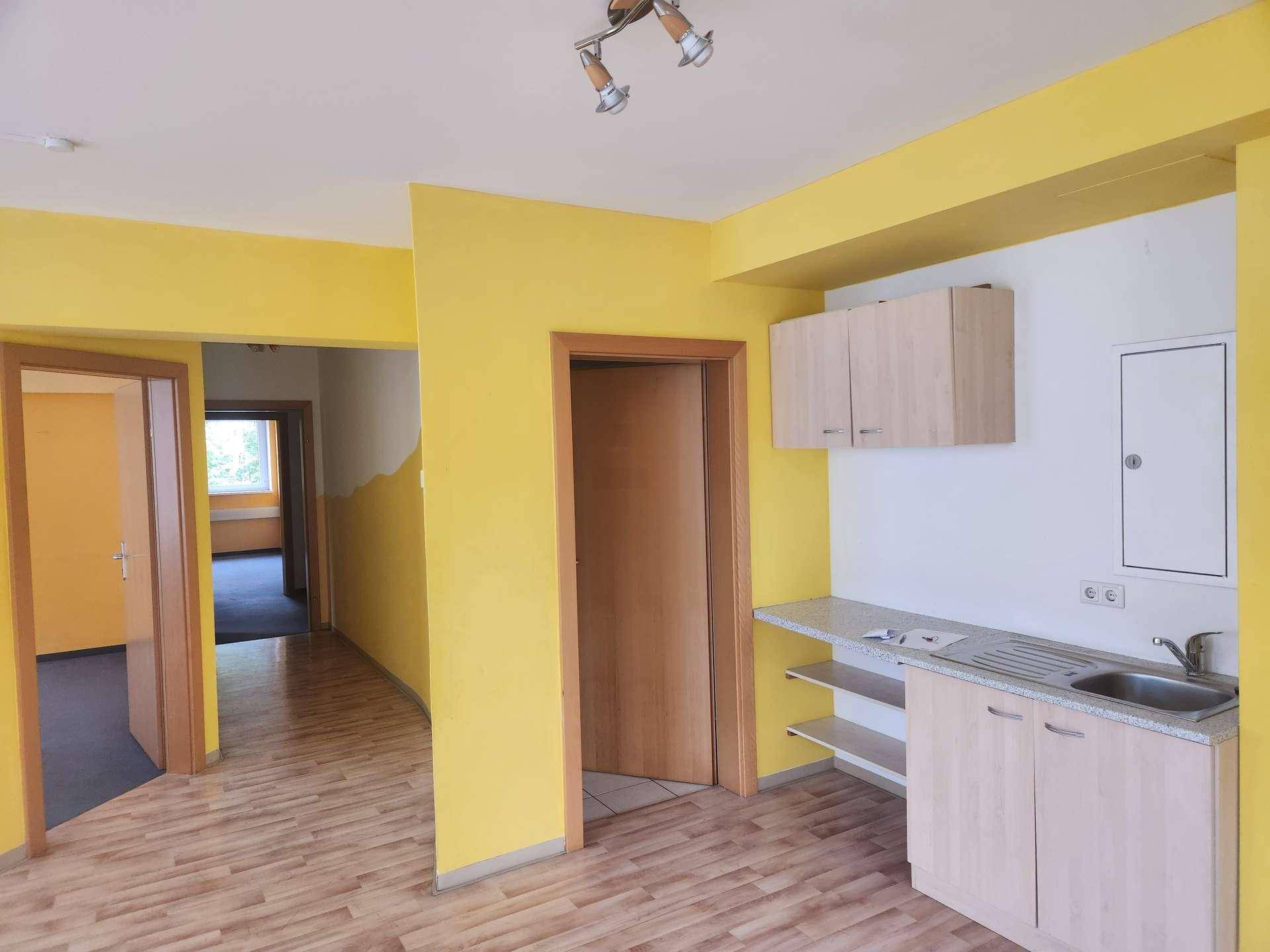 Heller Wohnbereich mit gelben Wänden, Laminatboden und einer integrierten, funktionalen Küchenzeile.