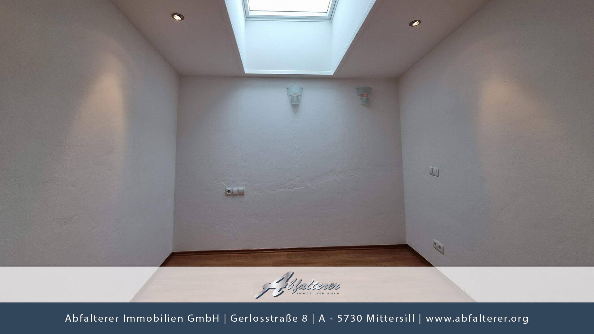 Leerer Raum mit weißen Wänden, Holzfußboden und einem Dachfenster für natürliches Licht.