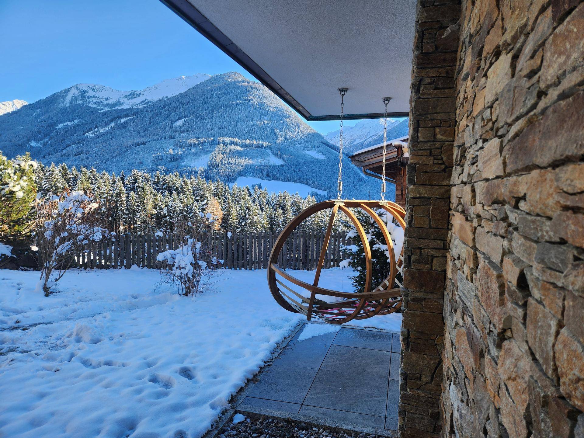 Verschneiter Gartenbereich mit Hängesessel und Blick auf die Berge und Wälder.