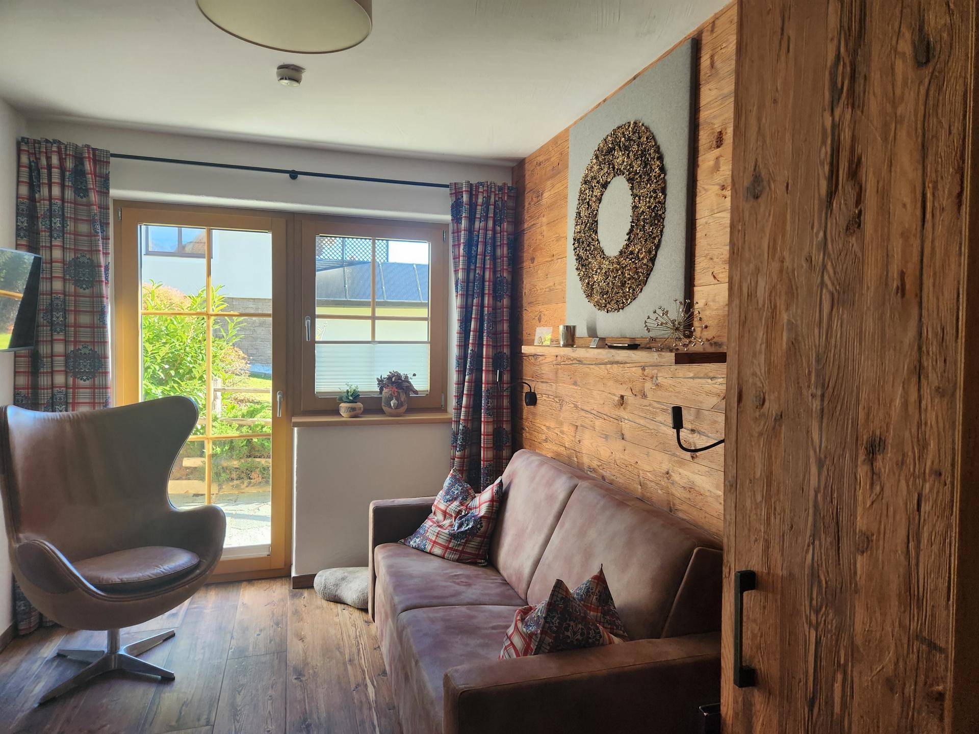 Gemütliches Schlafzimmer mit Holzboden, Sofa und Zugang zum Gartenbereich.