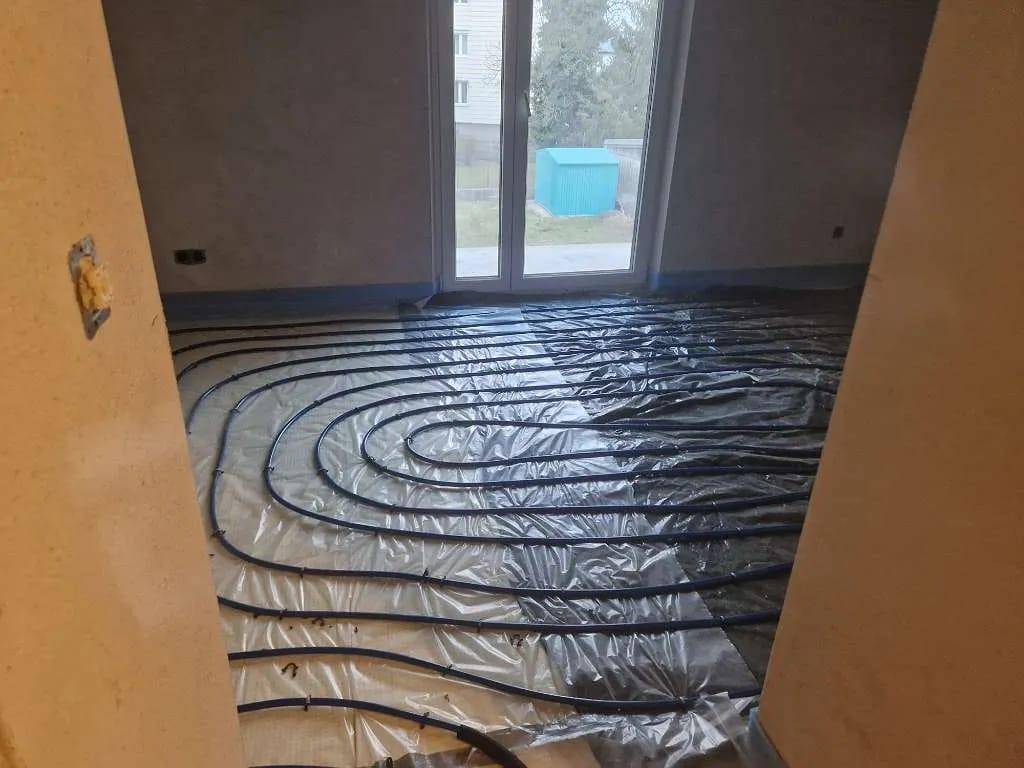 Raum im Bau mit verlegter Fußbodenheizung und einer großen Fenstertür zum Außenbereich.
