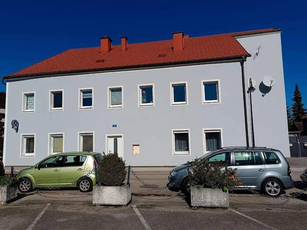 Vorderansicht des Gebäudes mit hellblauer Fassade, rotem Dach und geparkten Autos davor.