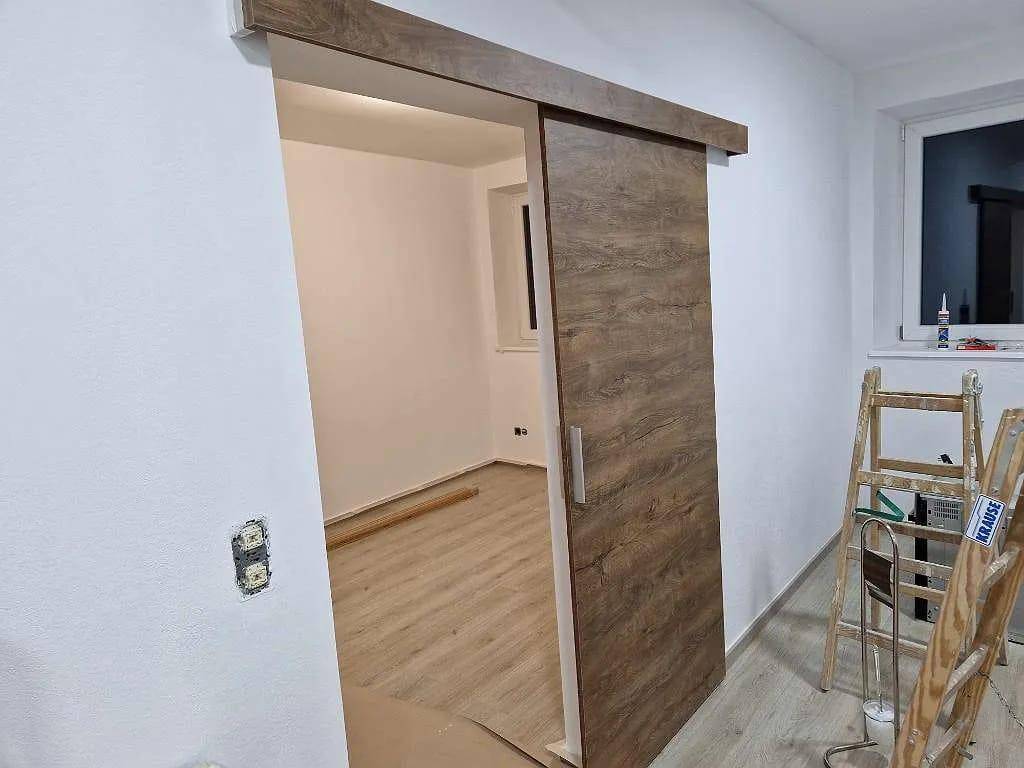 Moderner Innenraum mit einer Holzschiebetür und hellem Laminatboden im Bauzustand.