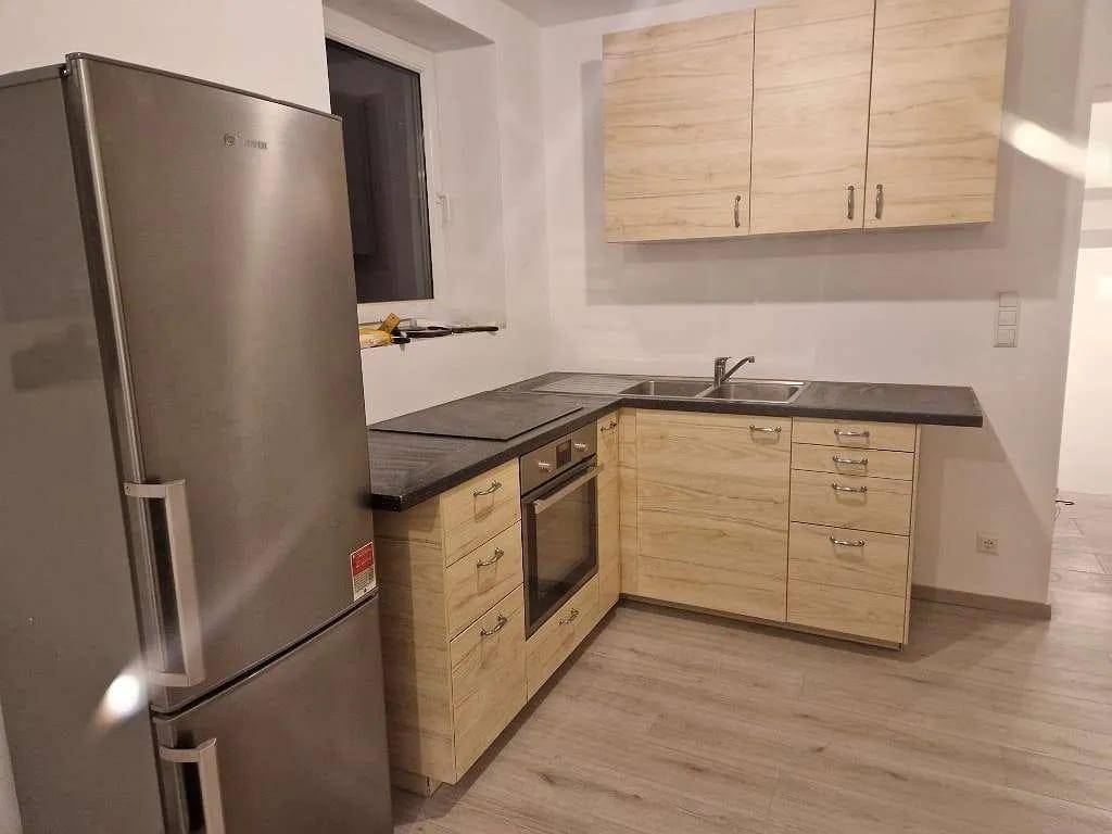 Moderne Einbauküche mit hellen Holzfronten, dunkler Arbeitsplatte und Edelstahlgeräten.